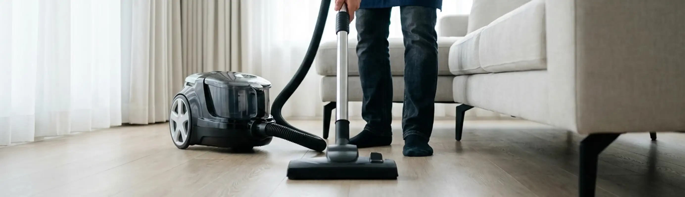 Professional house cleaner vacuuming a living room floor with a canister vacuum cleaner, Las Vegas, NV.