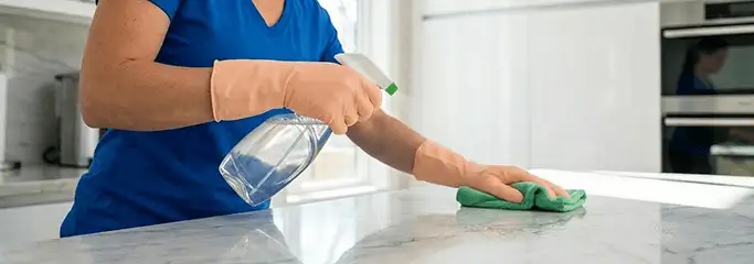 Maid service worker spraying and wiping a kitchen countertop with a microfiber cloth for sanitizing, Las Vegas, NV.