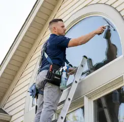 Professional window cleaner on a ladder using a squeegee to clean an exterior arched window, Las Vegas, NV.