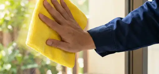 House cleaner wiping a glass window with a yellow microfiber cloth for streak-free cleaning, Las Vegas, NV.